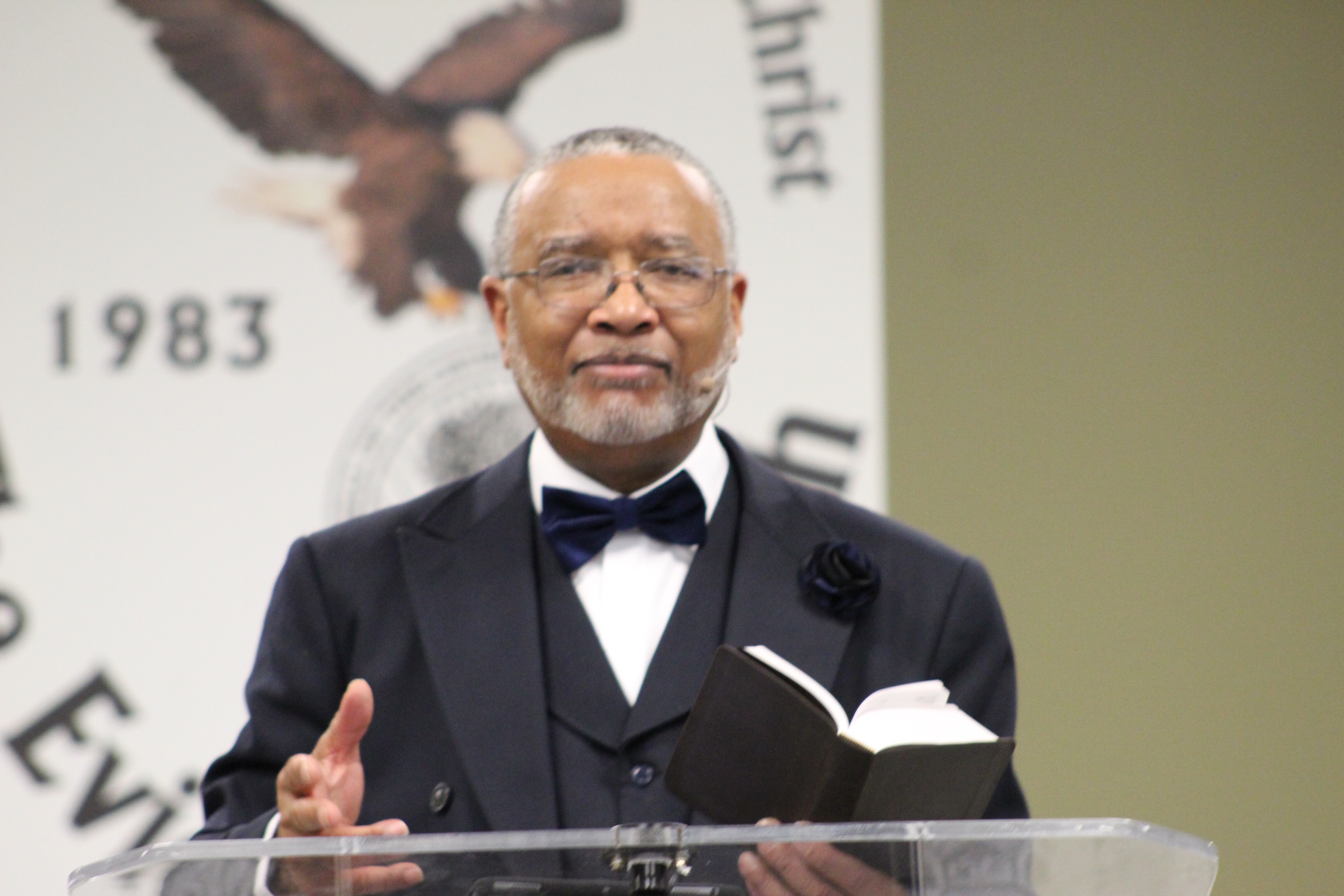 Dr. Gary L. Cordon, Sr. preaching holding Bible in left hand in front of logo in pulpit.